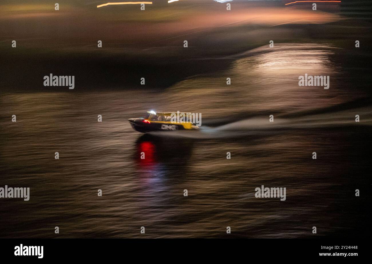 Water taxi speeds through the city river harbour at night, high speed blur panning shot Stock Photo