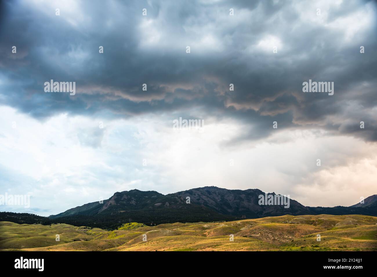 Dark, dramatic clouds gather over rolling hills and distant mountains. Stock Photo