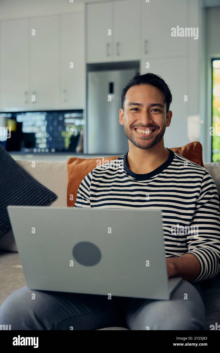 A man smiles while using a laptop computer on the couch Stock Photo
