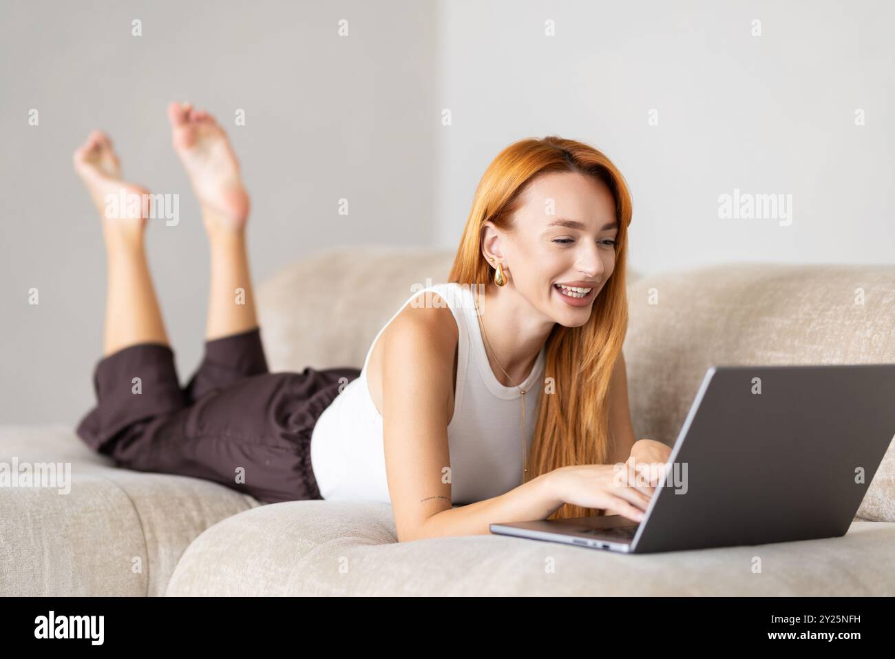 Young woman lying on couch with laptop Stock Photo - Alamy