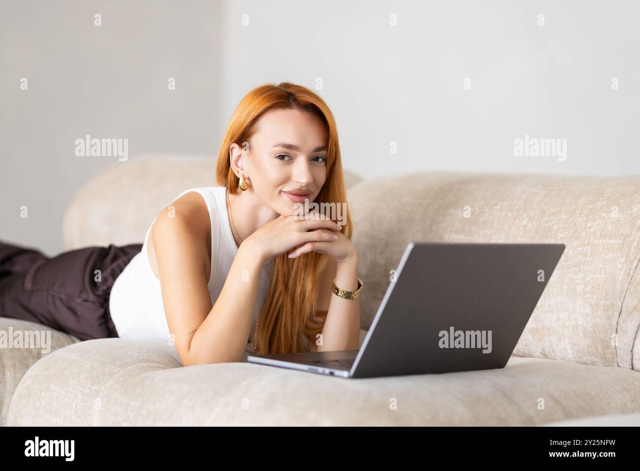 Young woman lying on couch with laptop Stock Photo - Alamy