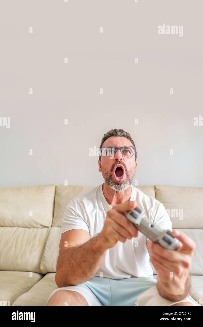 Front View of Excited Middle-Aged Man Enthusiastically Playing Video Games on His Sofa at Home Stock Photo