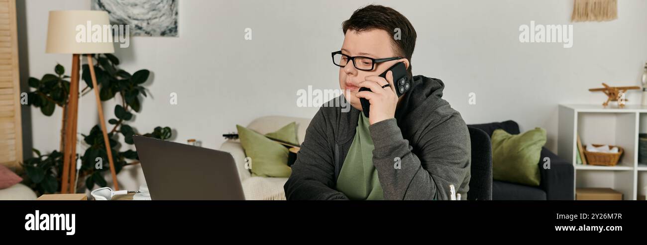 A young man with Down syndrome speaks on the phone while sitting at his desk. Stock Photo