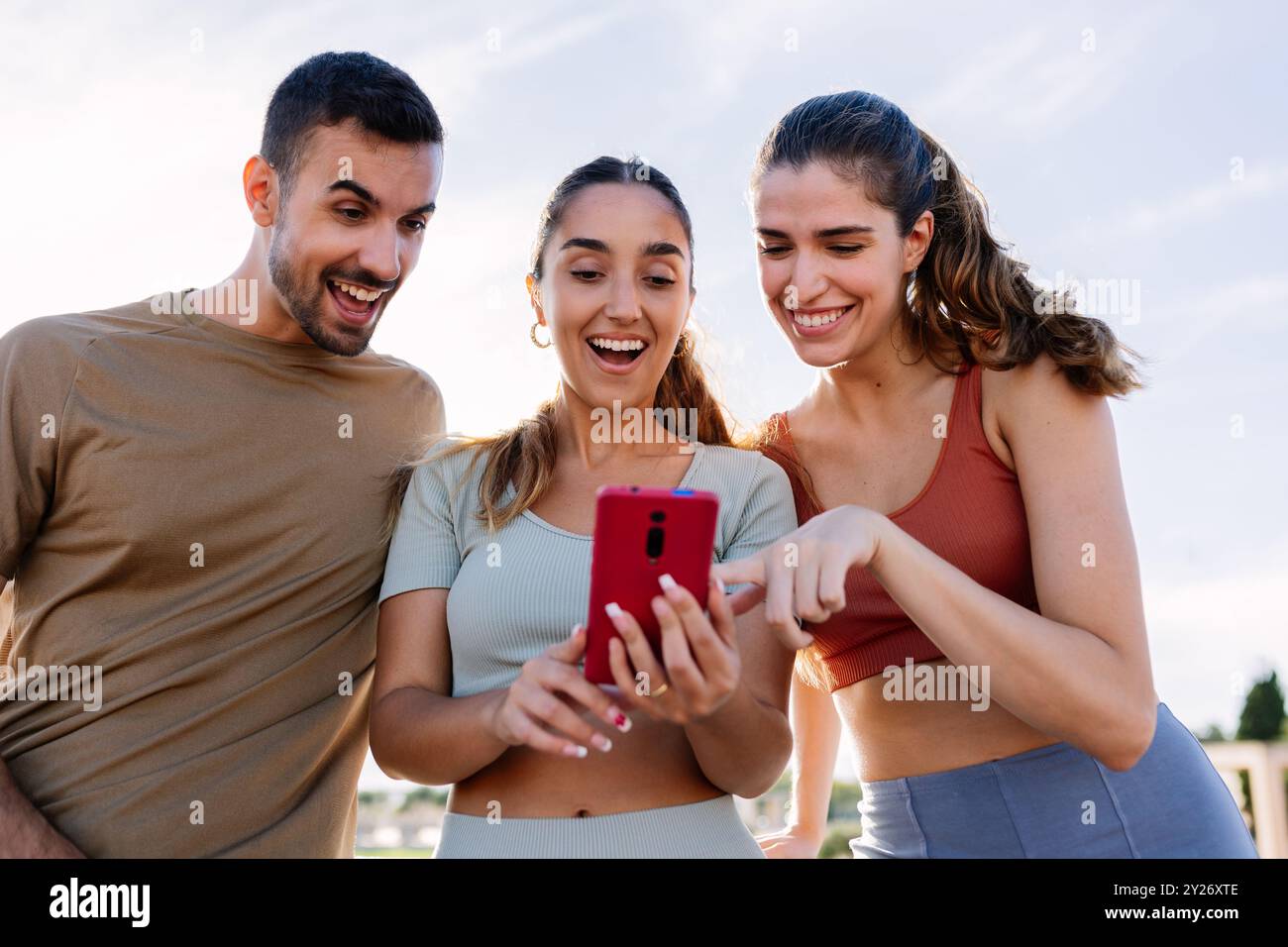 Three young sportive friends using mobile phone after workout routine outdoor Stock Photo
