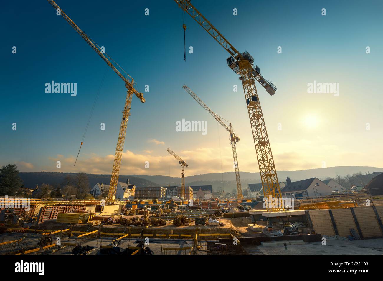 Large construction site with four yellow cranes looming into the blue sky with the sun and clouds. Wide angle tilted up view. Stock Photo