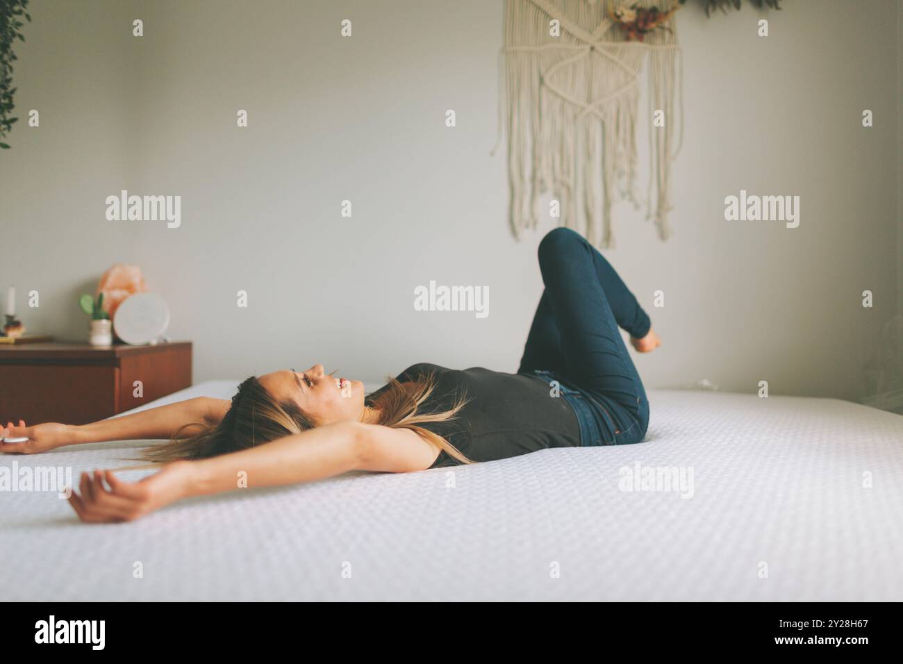 A woman relaxing on a bed in a bright white bedroom. Stock Photo