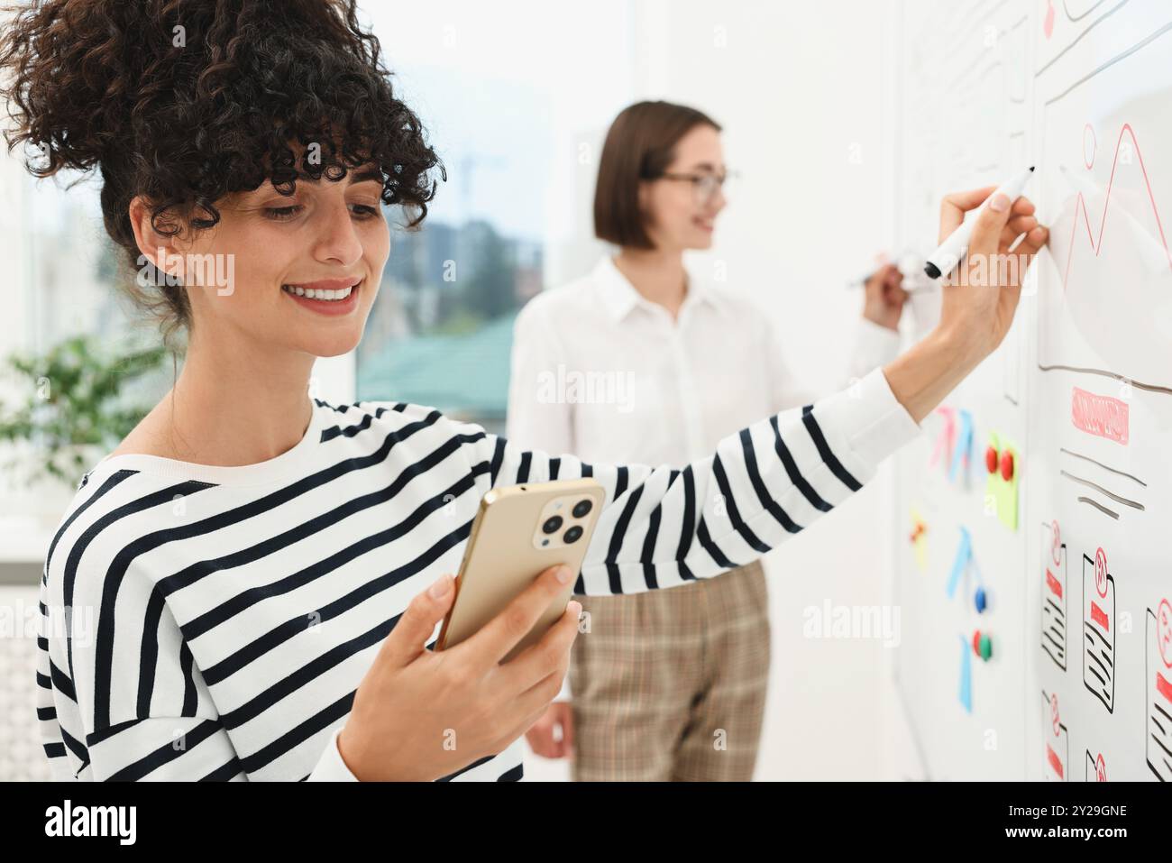 Developing UI design. Women drawing website wireframe on whiteboard indoors Stock Photo