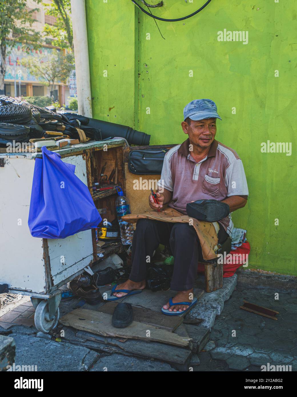 Balikpapan, Indonesia - June 22nd, 2024.  street vendor repairing shoes at an outdoor workshop. The image showcases the cobbler's tools, work in progr Stock Photo