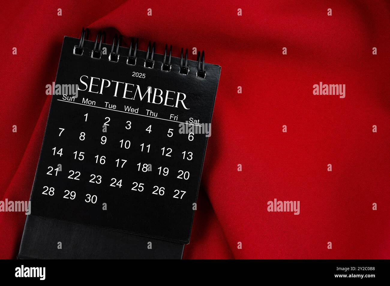 September 2025 Black spiral desktop calendar on red textile background