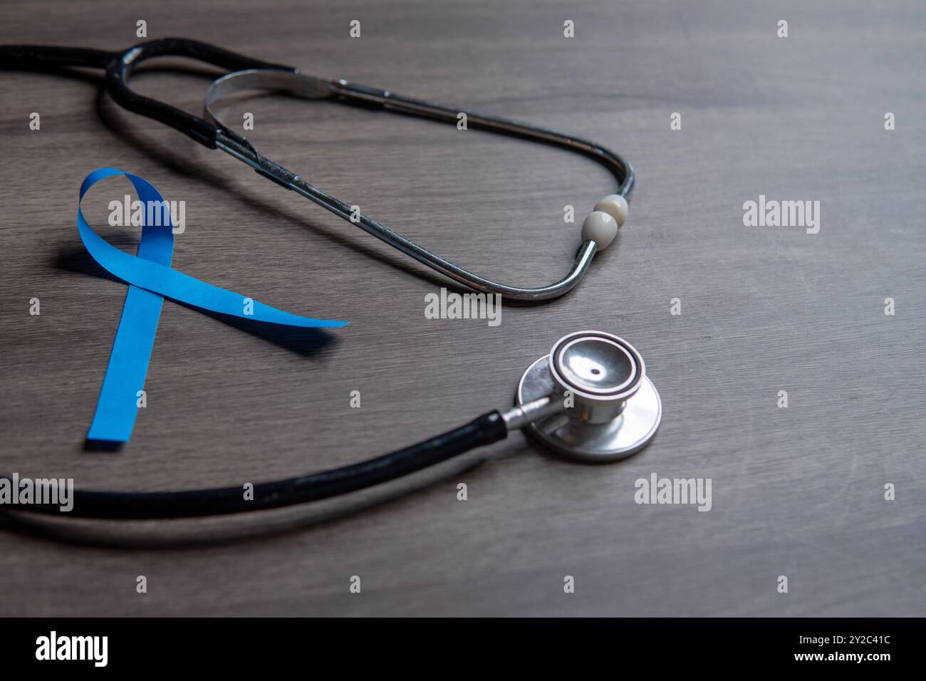 A blue ribbon and a stethoscope placed on a wooden surface. Men's health, prostate cancer awareness concept. Stock Photo