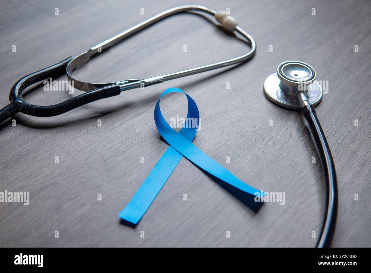 A blue ribbon and a stethoscope placed on a wooden surface. Men's health, prostate cancer awareness concept. Stock Photo