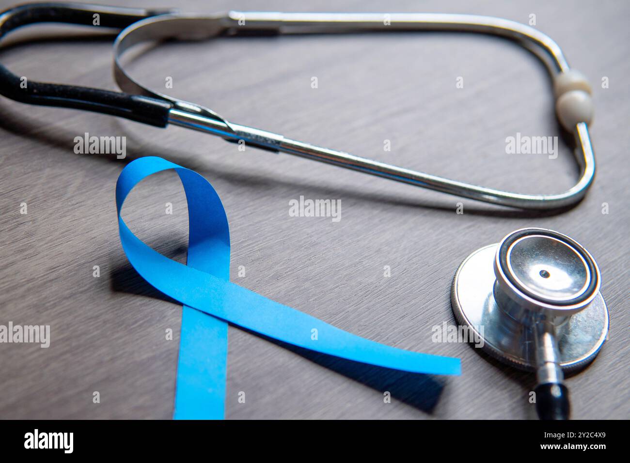 A blue ribbon and a stethoscope placed on a wooden surface. Men's health, prostate cancer awareness concept. Stock Photo
