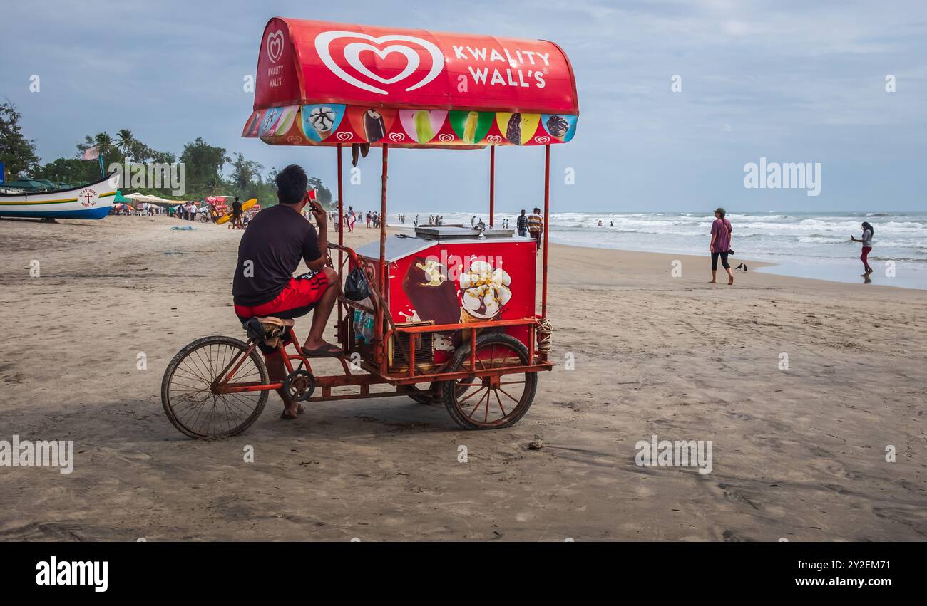Arambol beach, North Goa. Arambol beach with palm trees, beach umbrellas with Indian and foreign tourist. Indian man selling ice cream on tricycle. Tr Stock Photo