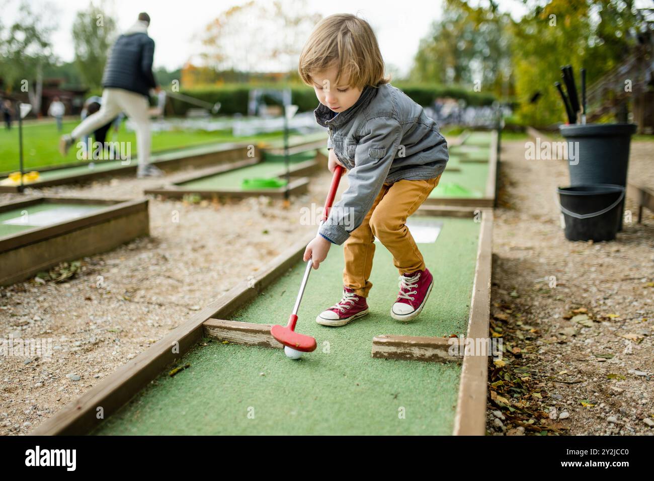 Cute toddler boy playing mini golf having fun on a playground outdoors on warm autumn day. Active leisure for kids in fall. Stock Photo