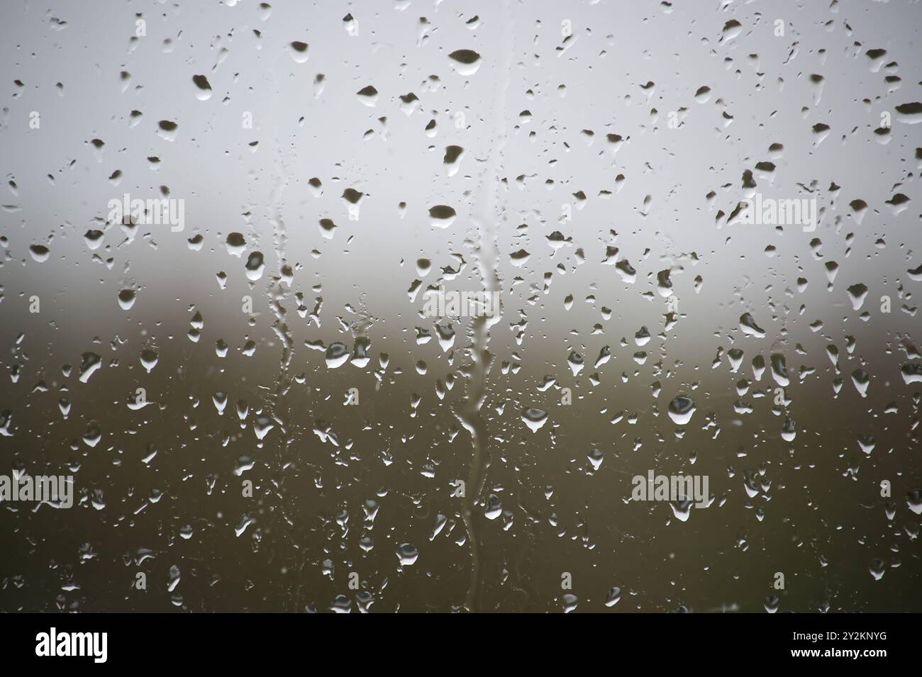 A window with raindrops on it. The raindrops are scattered all over the window, creating a blurry and hazy effect. Scene is calm and peaceful, as the Stock Photo