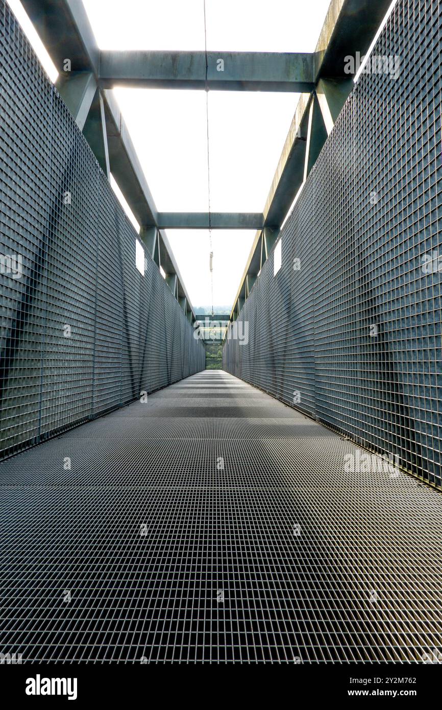 A wide walkway features grid flooring and an open structure above, creating a unique perspective in an industrial environment. Sunlight illuminates th Stock Photo