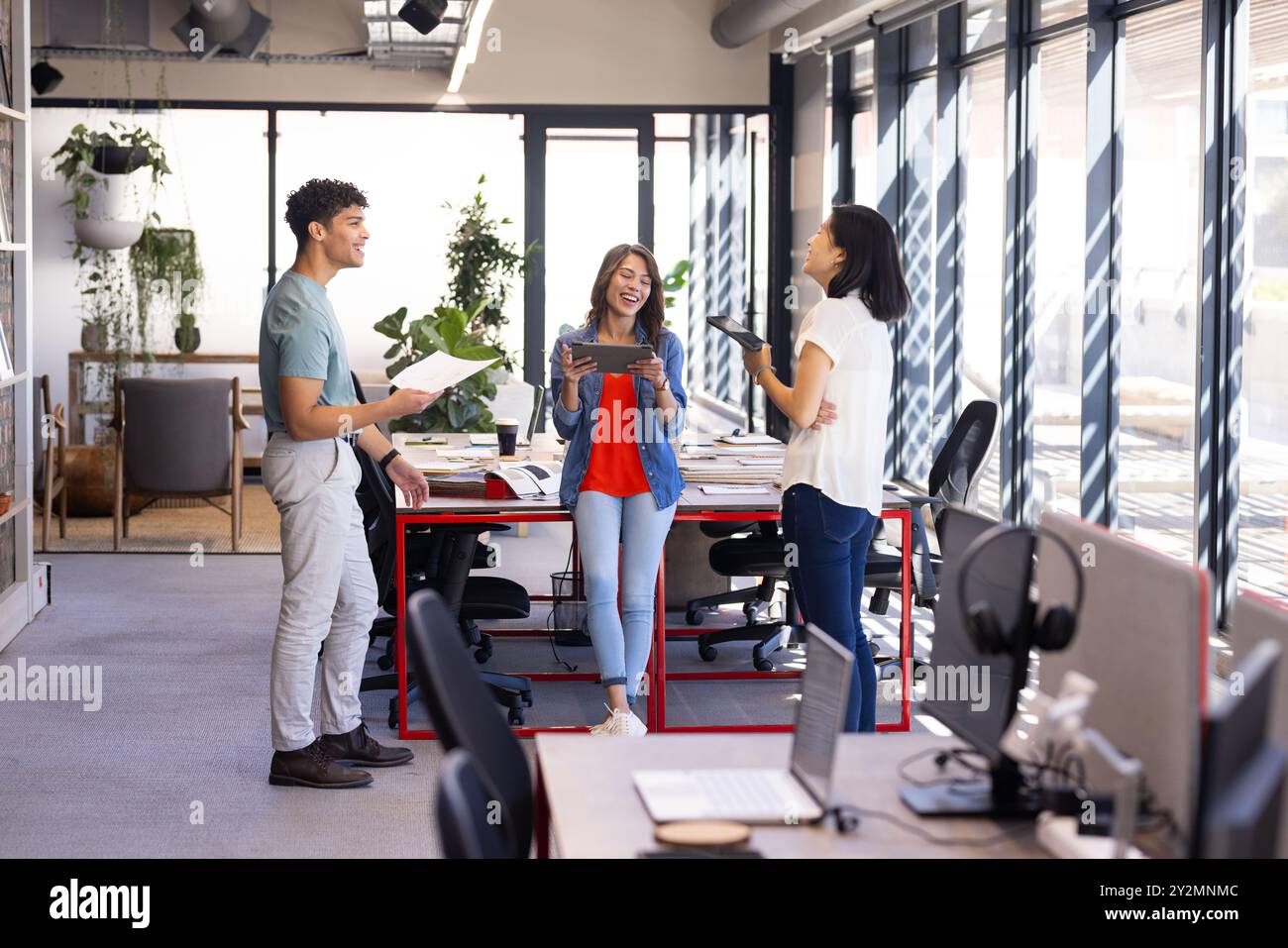 Discussing project details, diverse colleagues using digital tablets in modern office setting Stock Photo