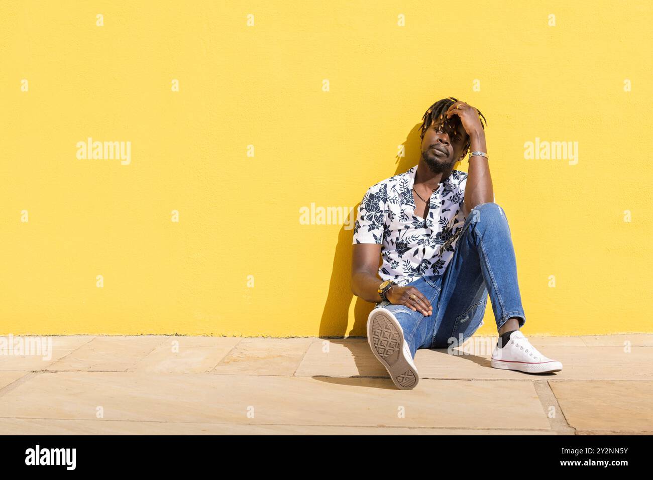 black man sitting on the floor against yellow wall Stock Photo