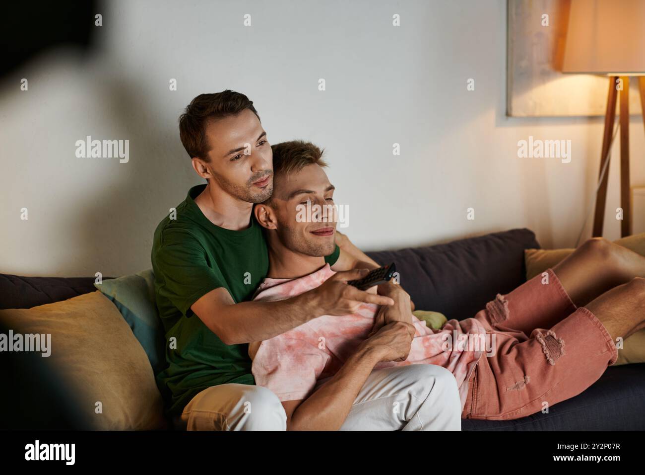 Two men share joy and laughter while cuddling on the couch. Stock Photo
