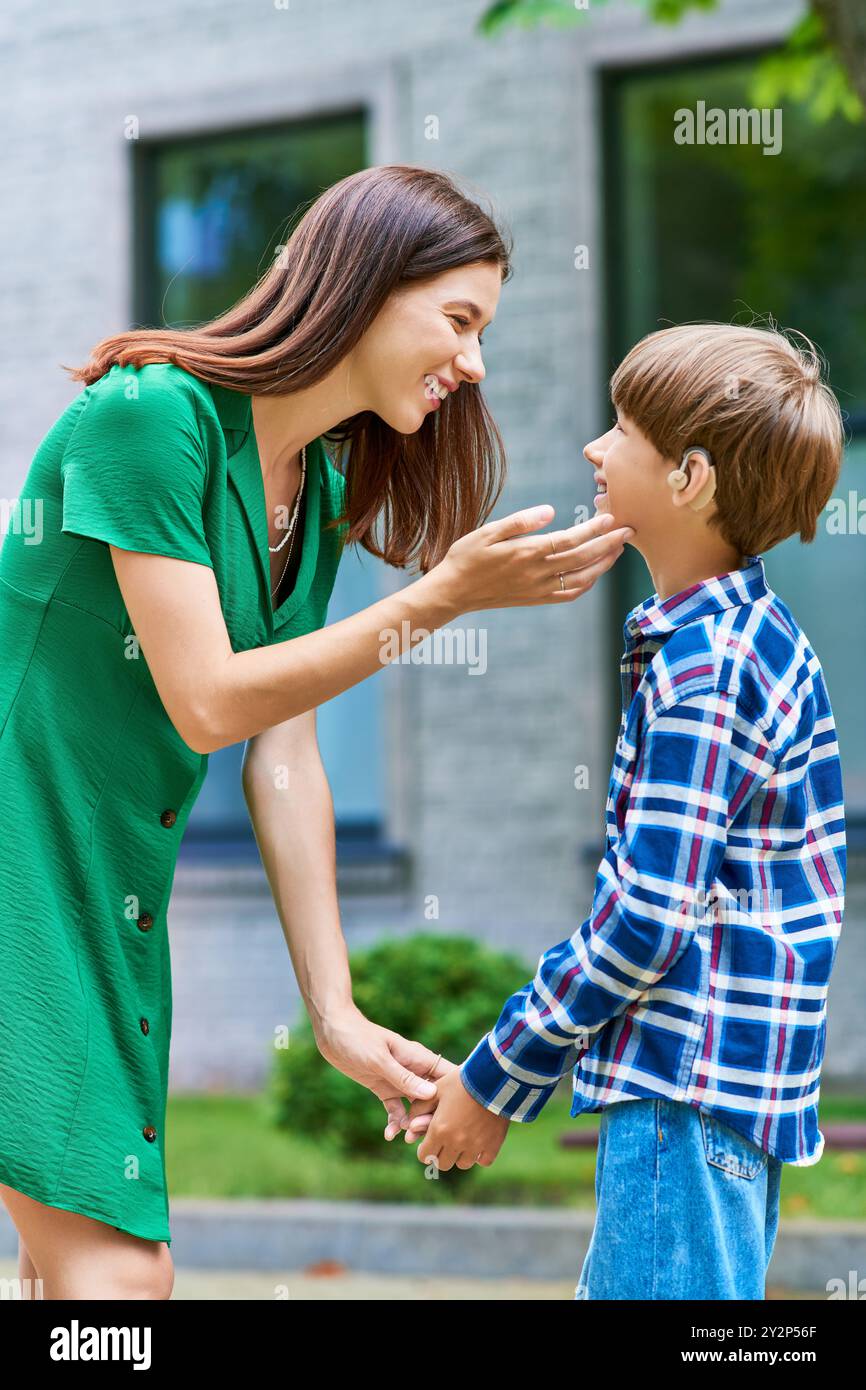 A mother lovingly interacts with her hearing impaired son in a sunny garden. Stock Photo