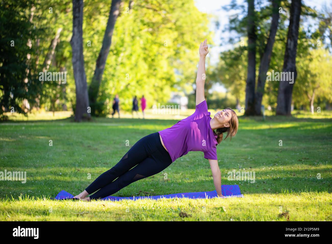 Woman leading a healthy lifestyle, doing yoga in the park, doing Vasishthasana exercise, side plank pose on outstretched arms, training alone in sport Stock Photo