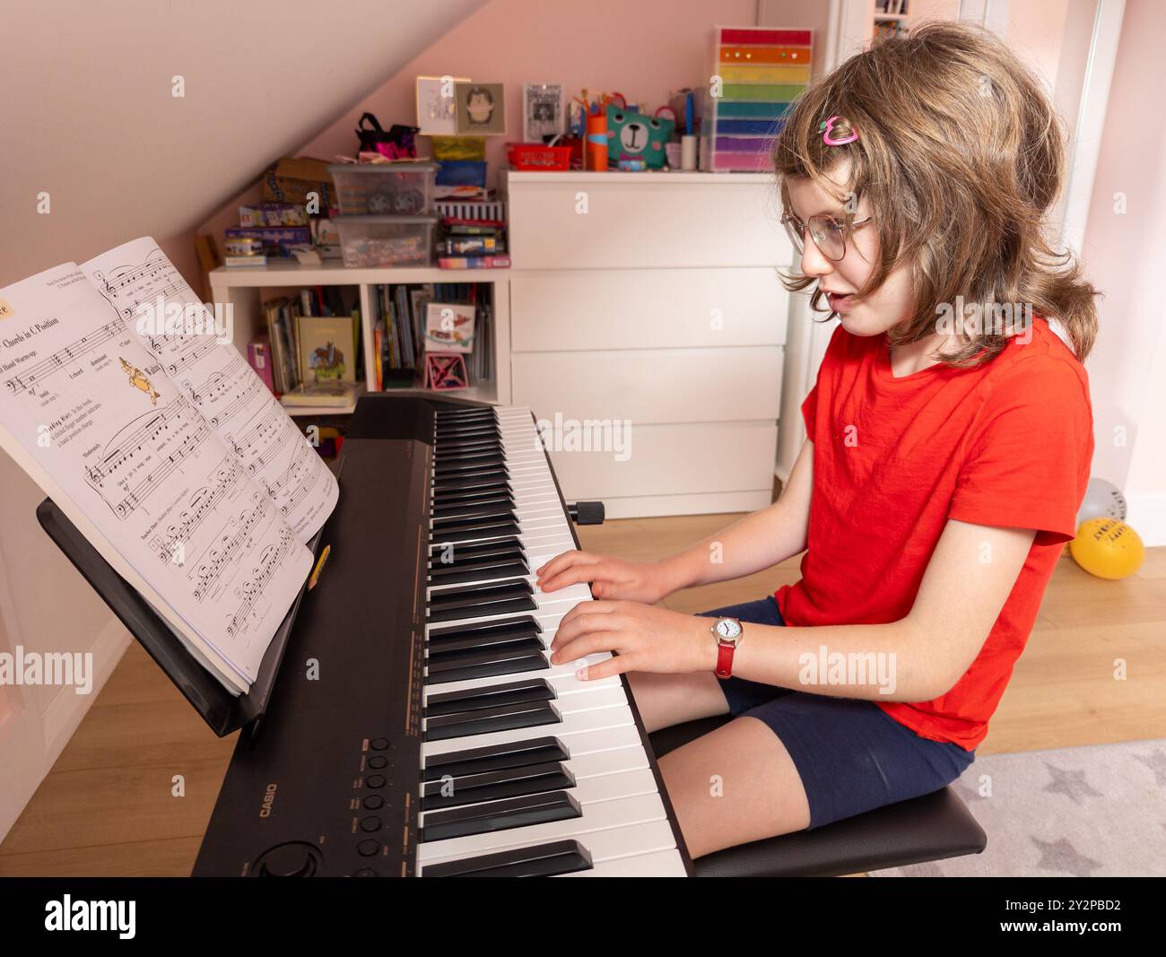 Young 10 year old girl playing on her electric piano in her bedroom at home, UK Stock Photo