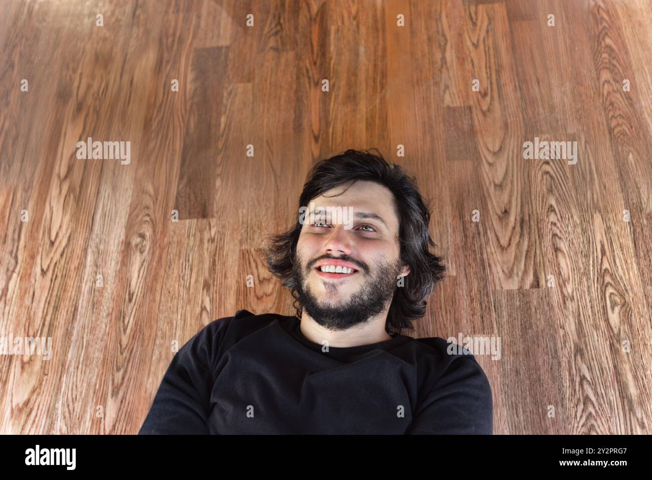 single happy young man with a beard laying down on a wooden floor Stock Photo