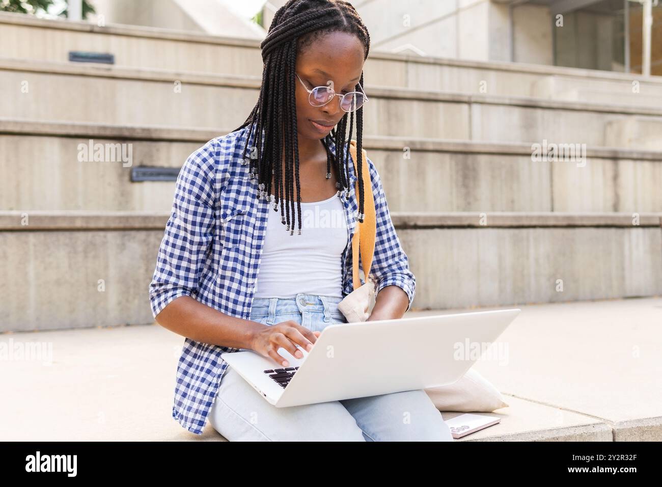 A focused black woman sits outdoors in a business district, using her ...