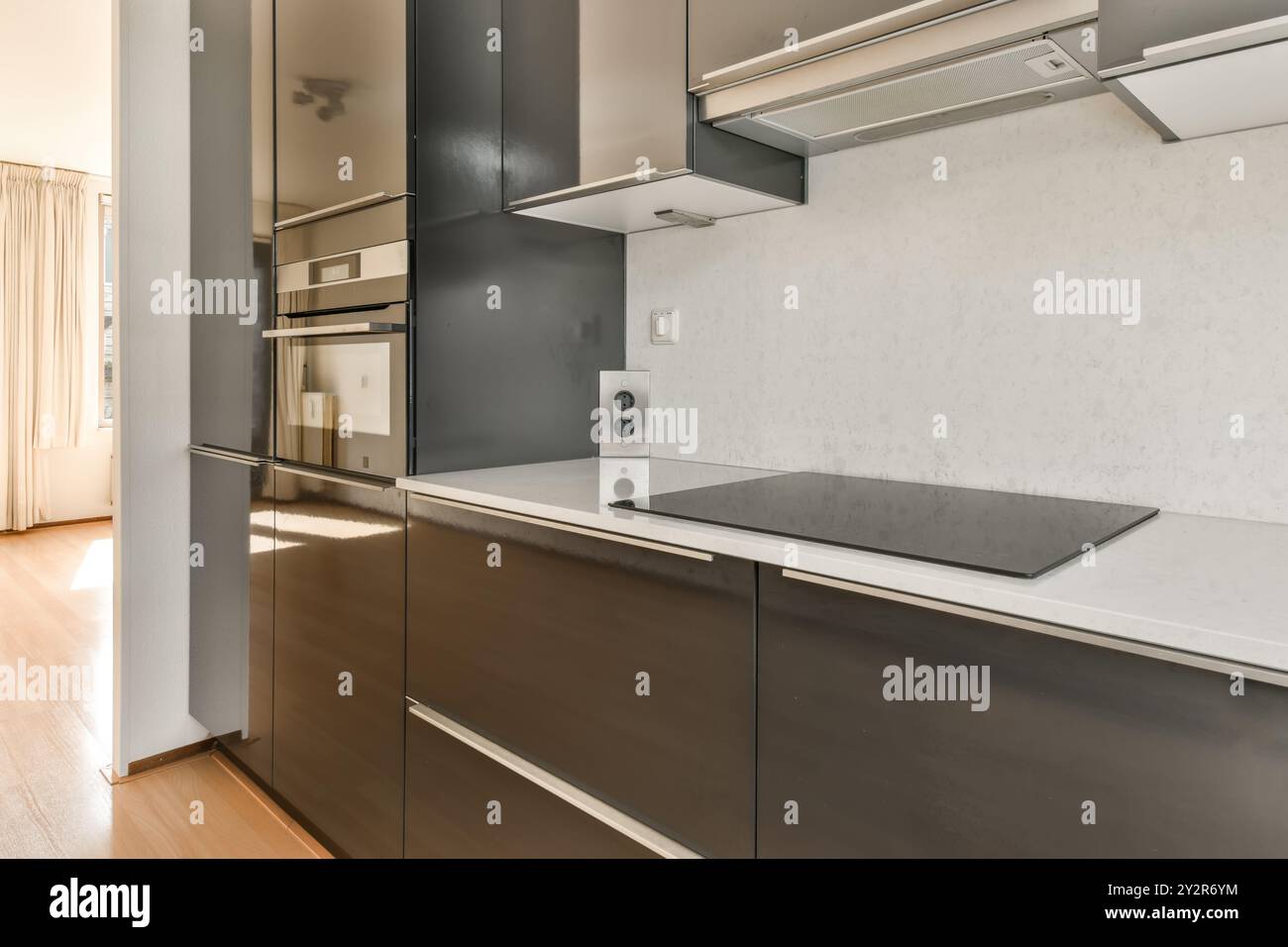 A contemporary kitchen featuring dark cabinets, a built-in oven, and a ...