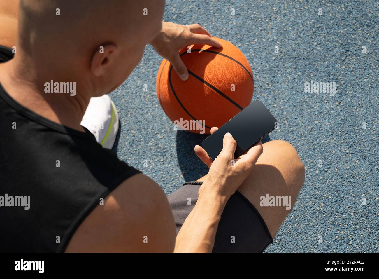 Basketball player using smartphone and texting social media during game interval, Outdoor training. View from above. Stock Photo