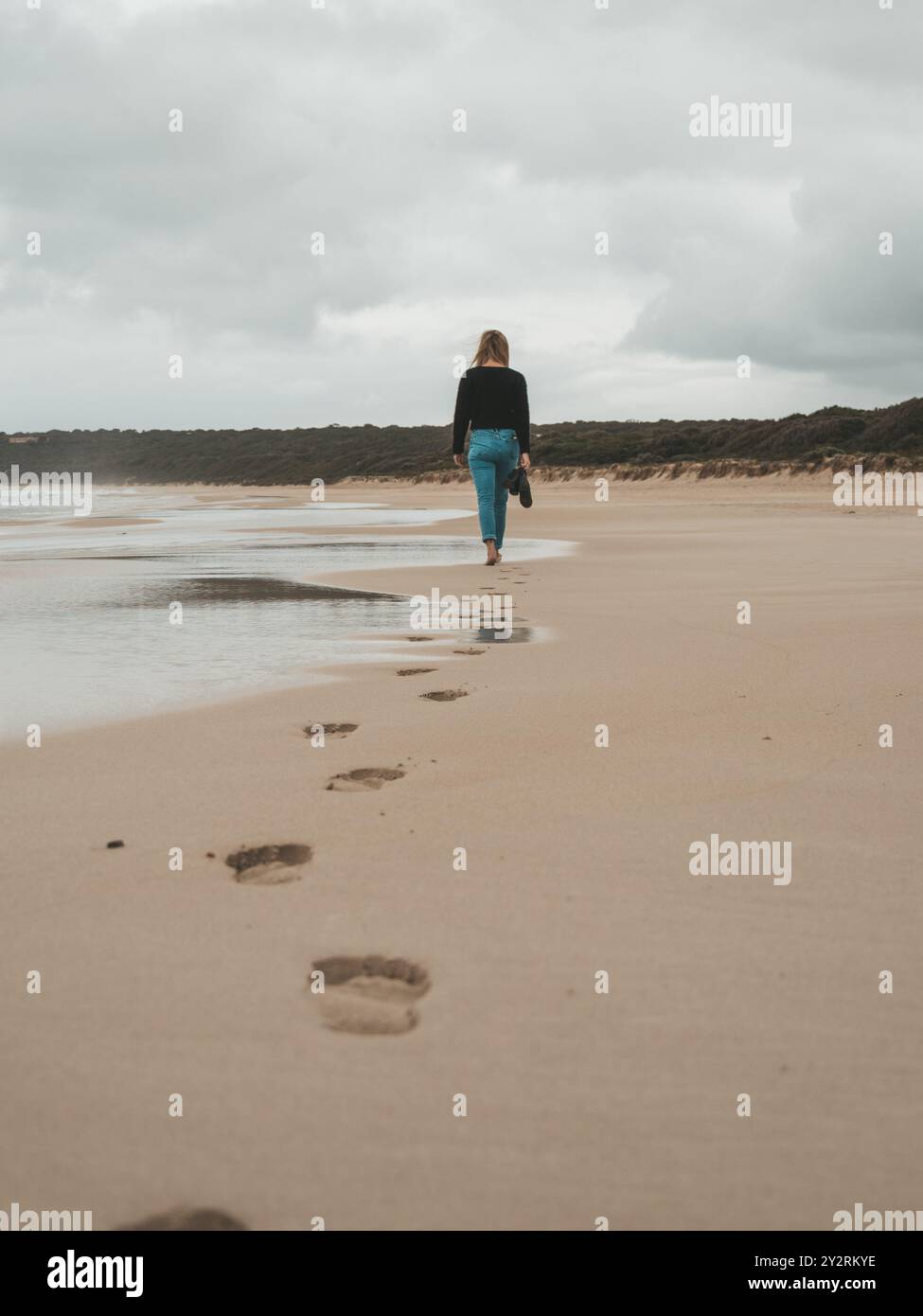 A woman walking barefoot on a sandy beach leaving footprints behind on ...
