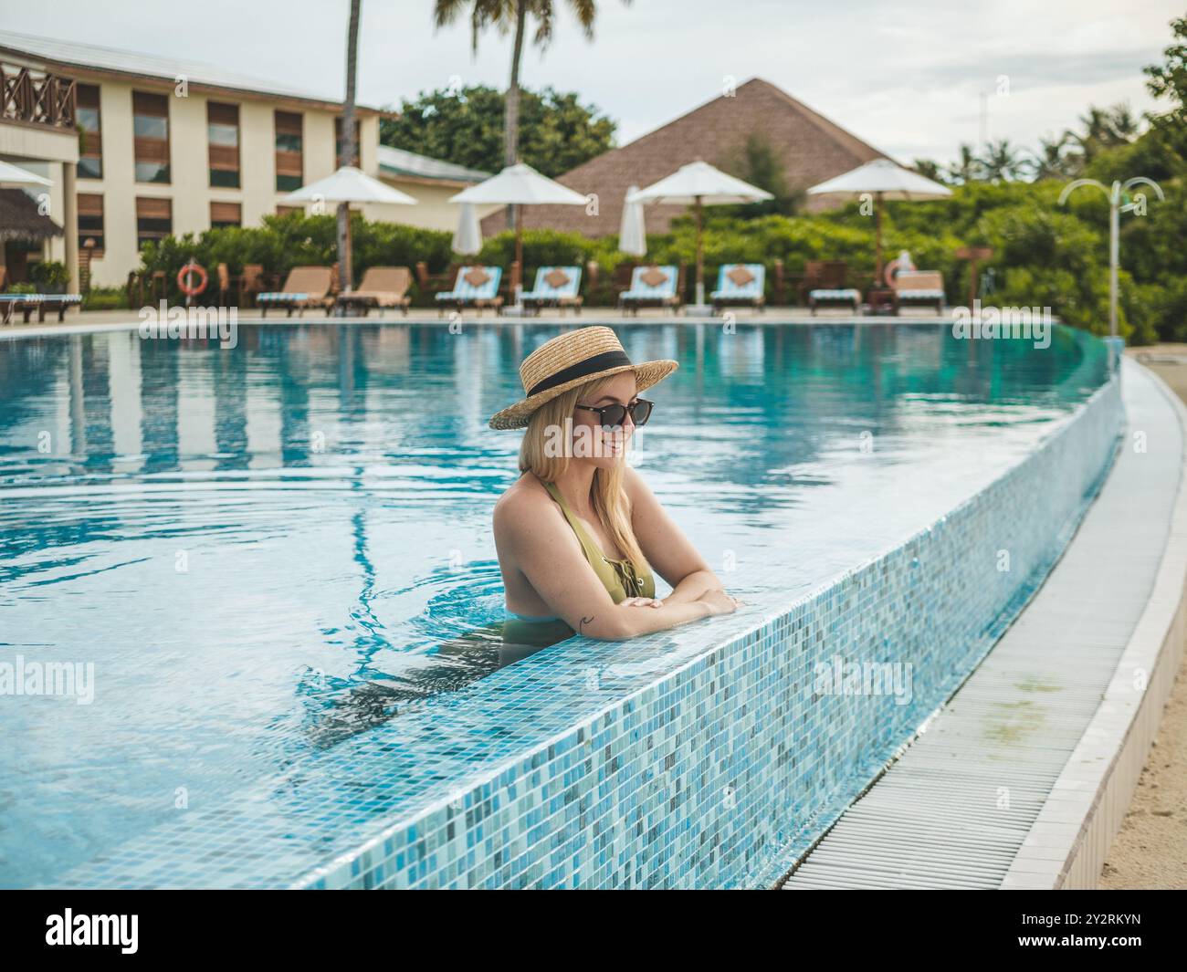 A young woman in a straw hat and sunglasses relaxing in an infinity ...