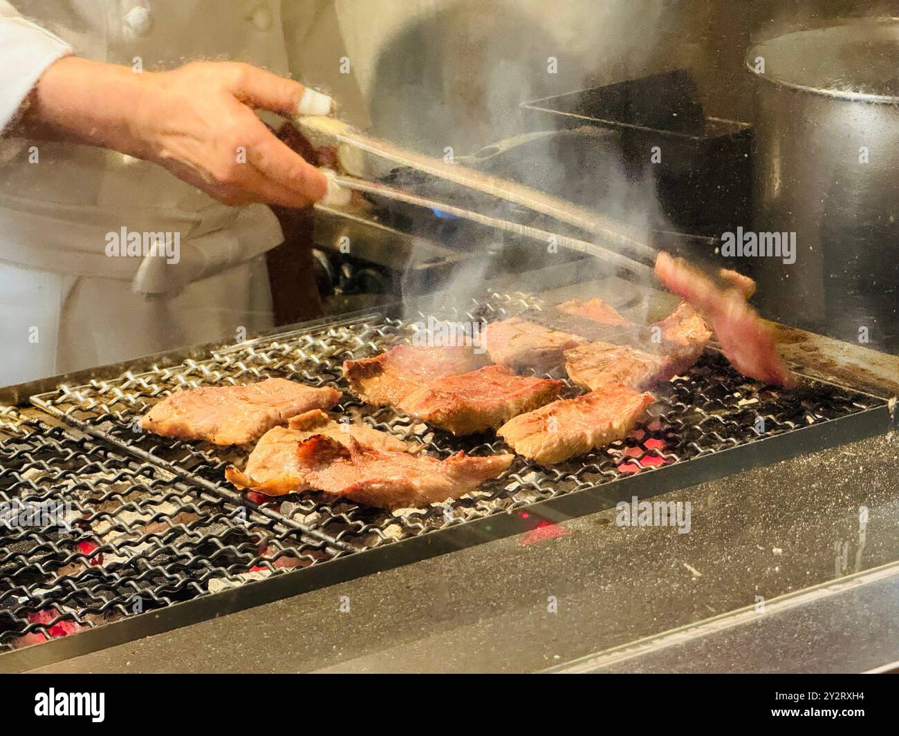 Chef grilling beef steaks on a barbecue grill in a restaurant kitchen Stock Photo