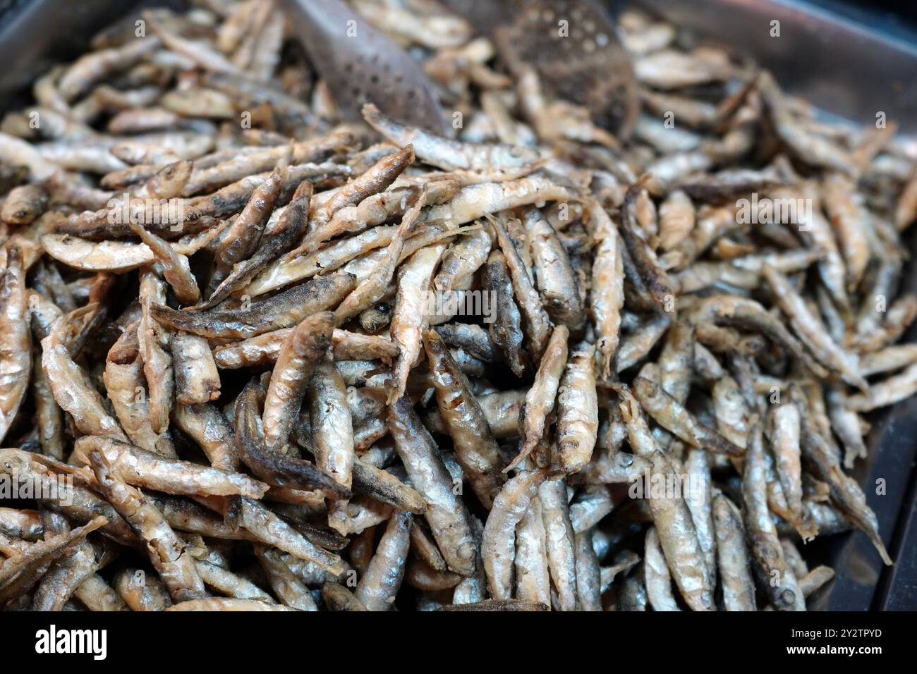 Pile of fried salty anchovies in metal griddle at street food fair 