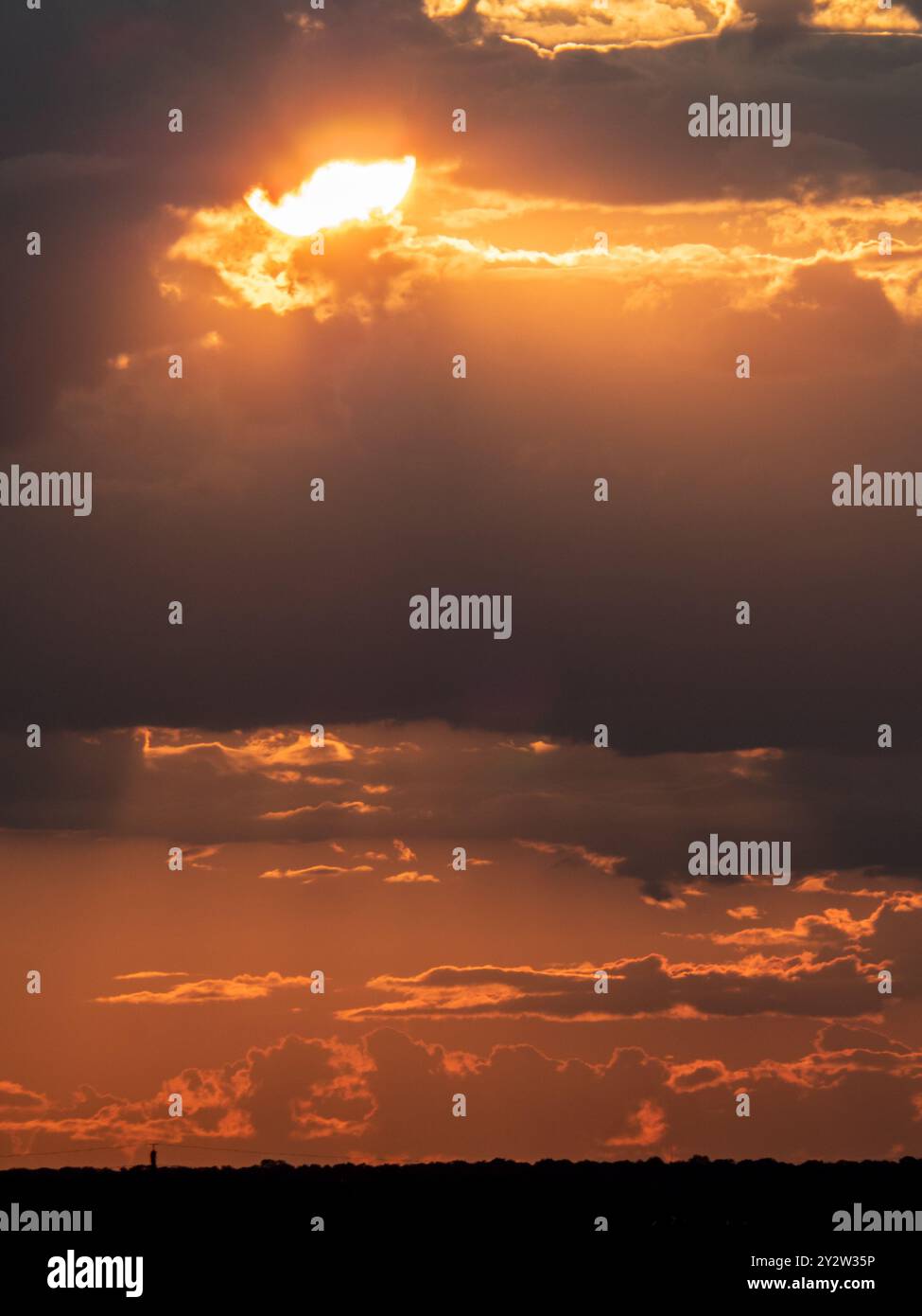 A dramatic sunset with fiery clouds and the sun peeking through ...
