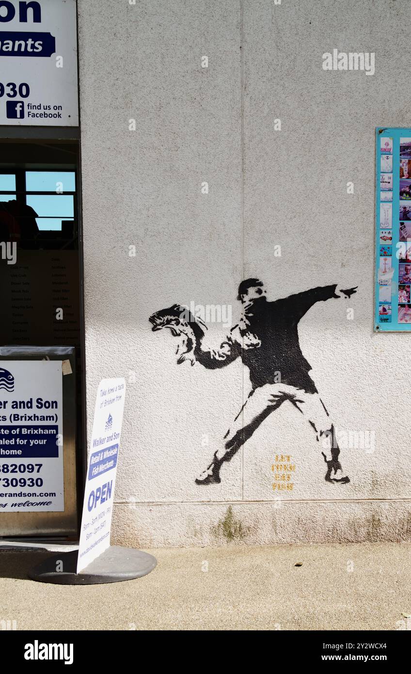 Street Art Of A Man IN Bandana Face Mask Throwing A Fish, Let Them Eat Fish, Ouside A Seafood Vendors Shop, Brixham Devon UK Stock Photo