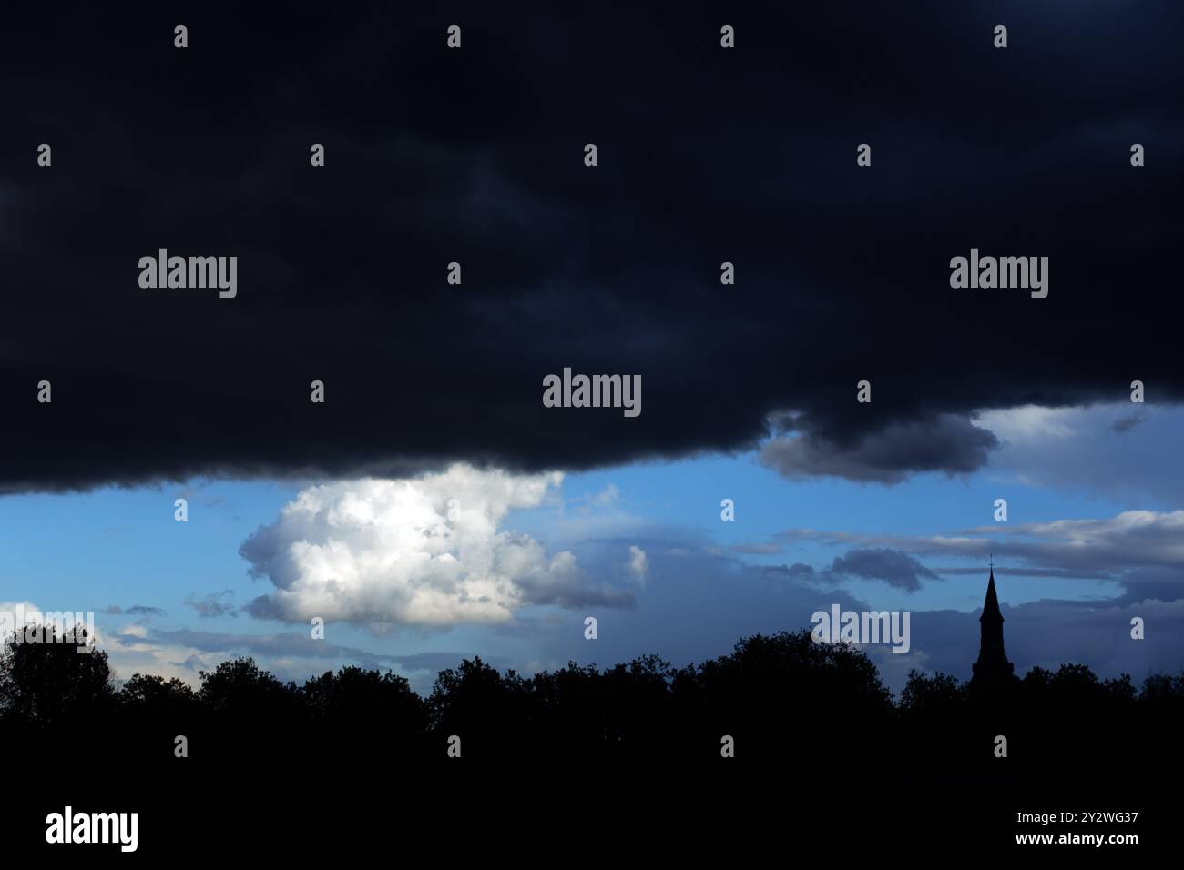 Treetops and church tower silhouetted against black nimbostratus cloud bringing rain in late summer Stock Photo