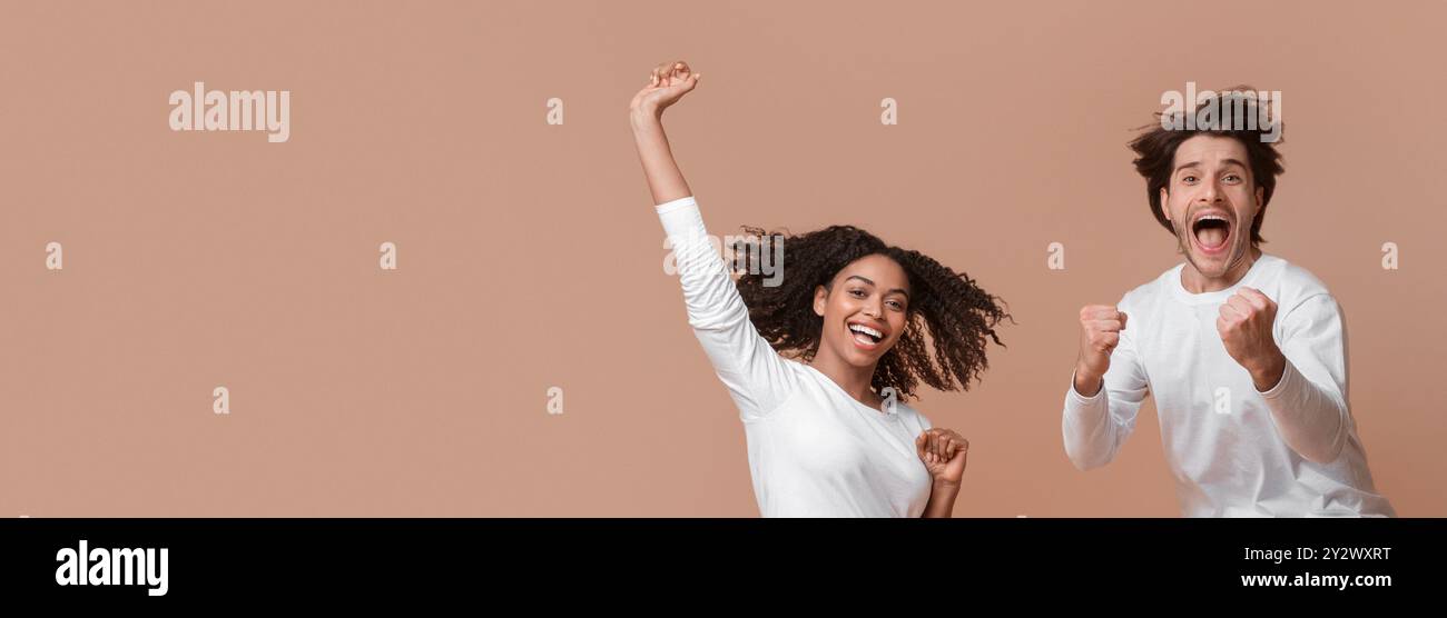 Overjoyed multiracial couple jumping in the air and celebrating success Stock Photo