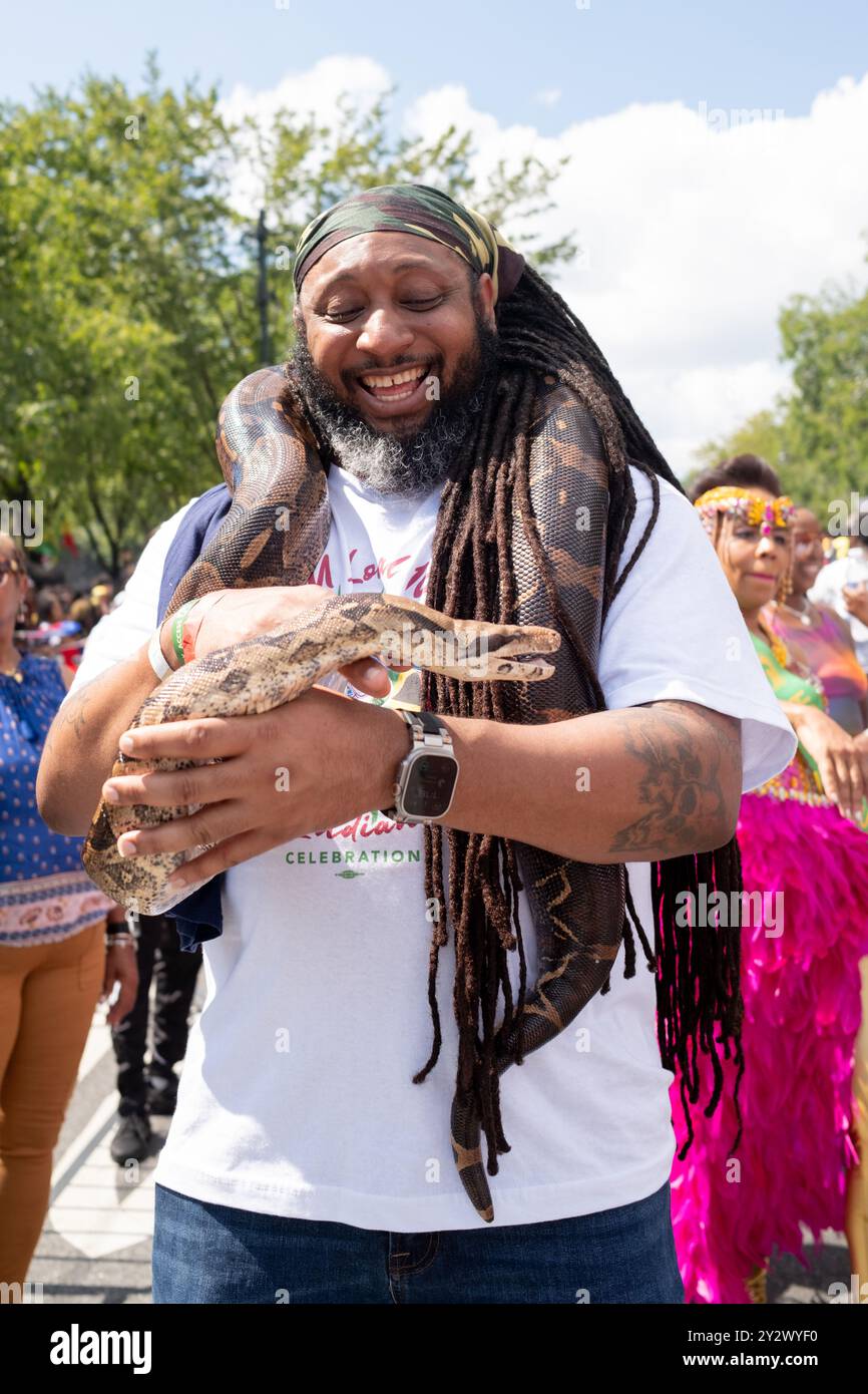 a cheerful man is holding a large snake wrapped around his neck and arms, participating in the festivities. Stock Photo
