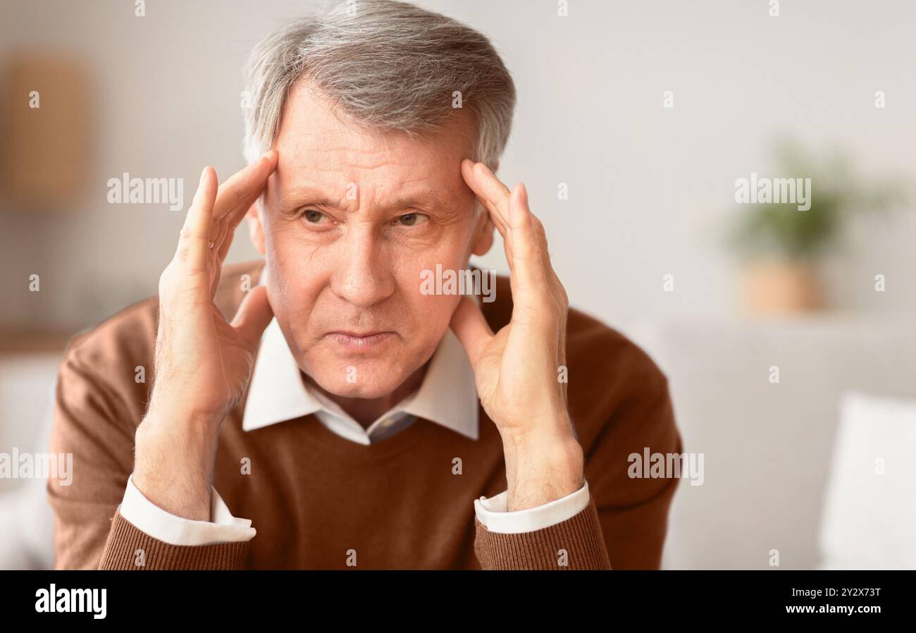 Elderly Man Having Headache Touching Temples Sitting On Couch Stock Photo