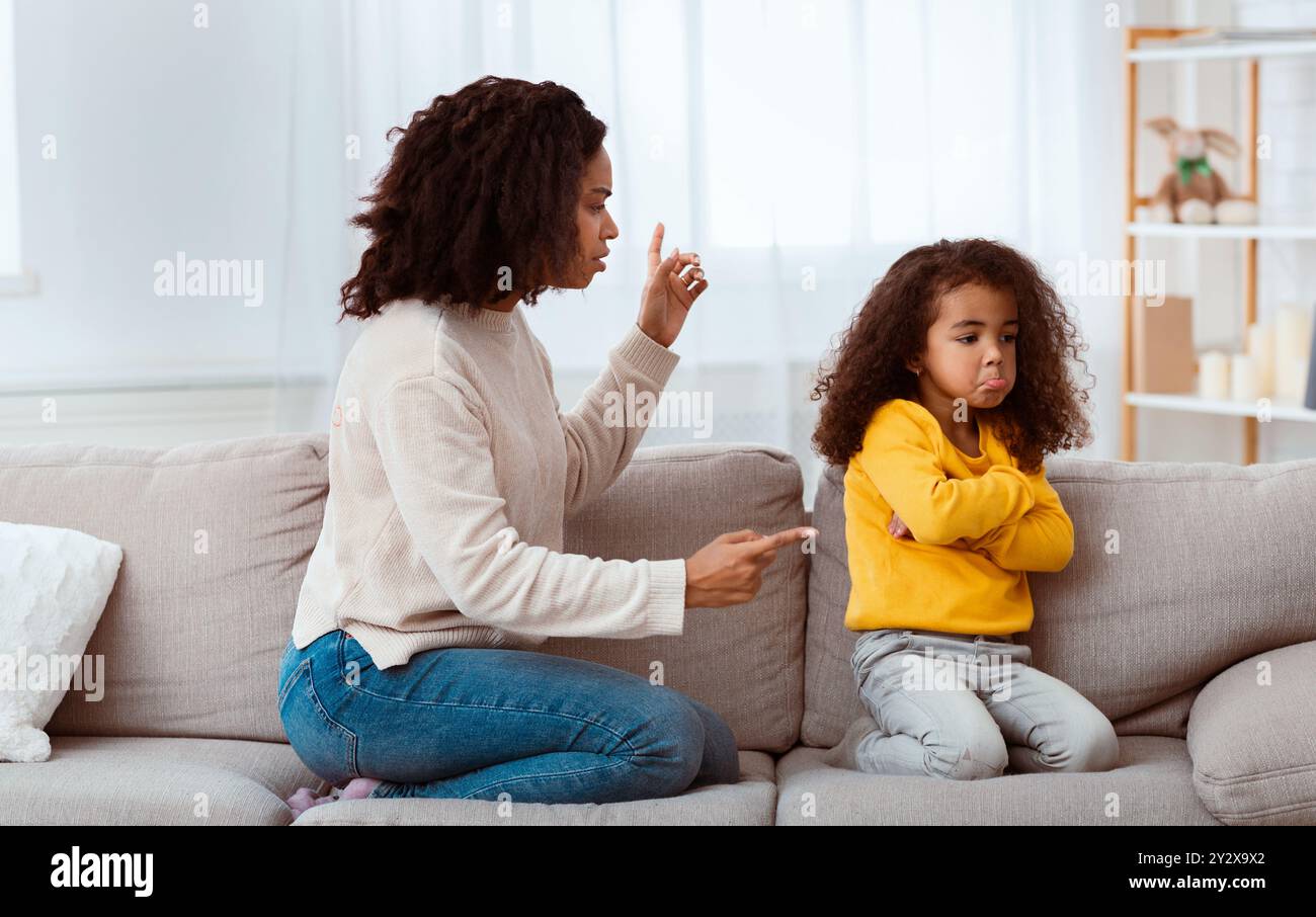 Black Mother Scolding Daughter Sitting On Sofa At Home Stock Photo