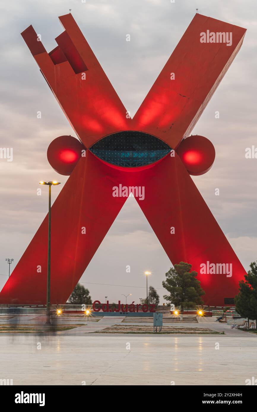 The iconic X sculpture in Ciudad Juarez, Mexico, illuminated at dusk with a cloudy sky background. Stock Photo