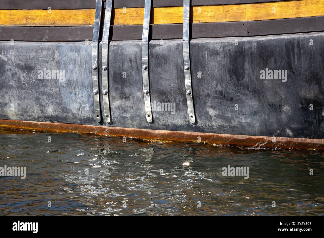 Close-up of a boat's hull showing metal fastenings and wooden accents, partially submerged in water. Stock Photo