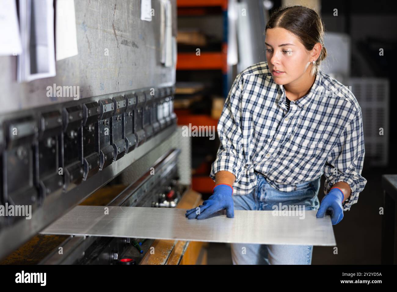 Young woman placing metal sheet on bending machine in workshop Stock Photo