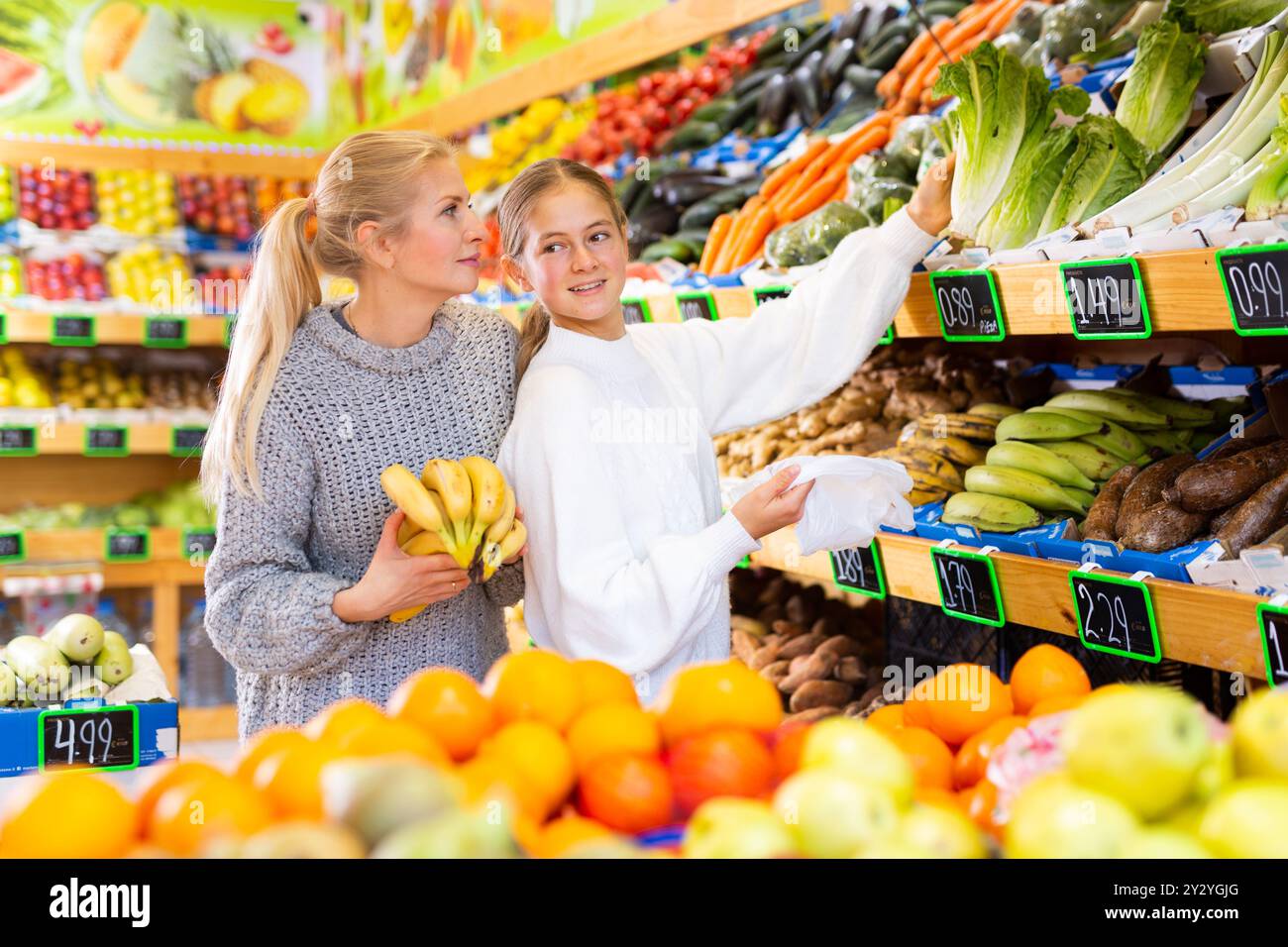 Portrait of teenage girl and mother who buying fresh vegetables and ...