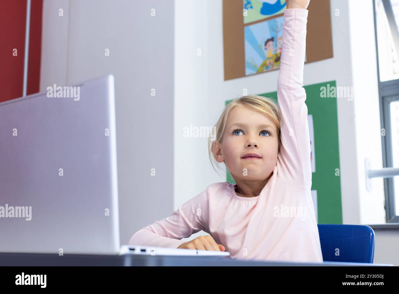 In school, girl raising hand while sitting at desk with laptop Stock ...
