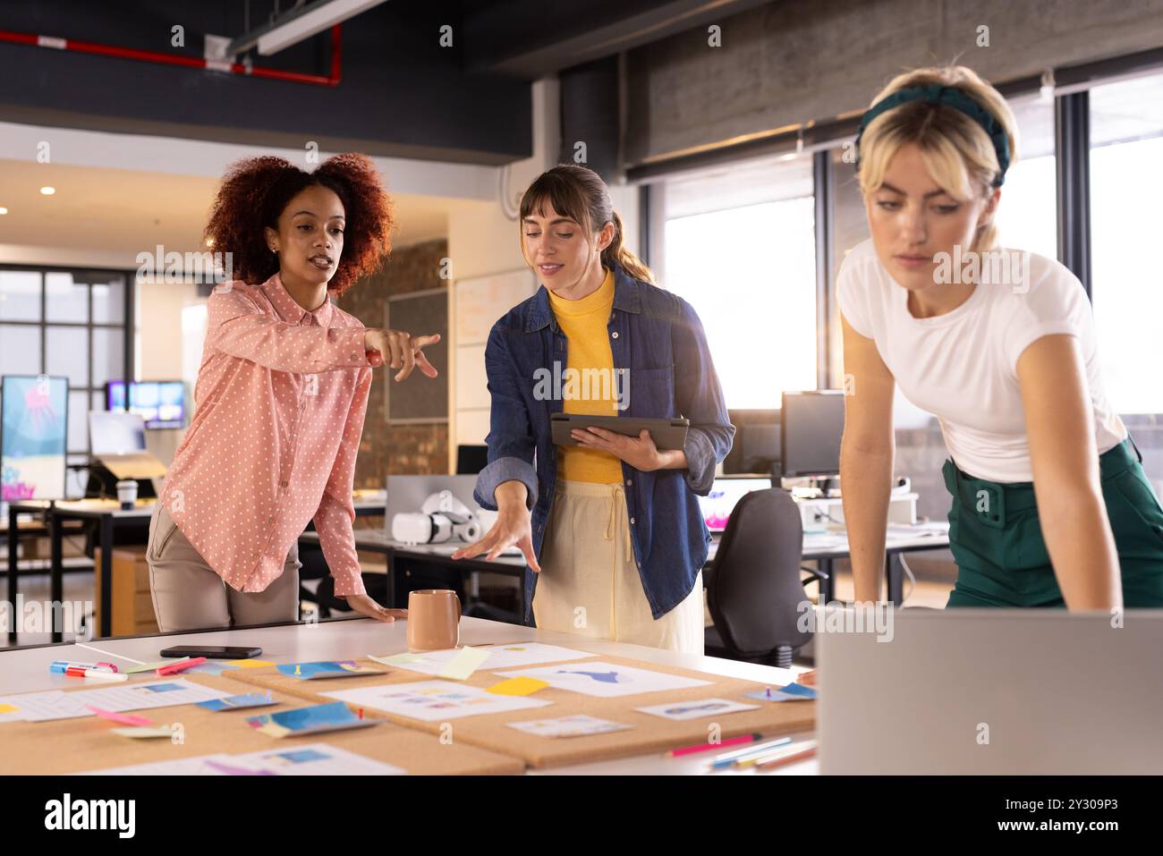Collaborating on creative writing project, three multiracial women discussing ideas in office Stock Photo