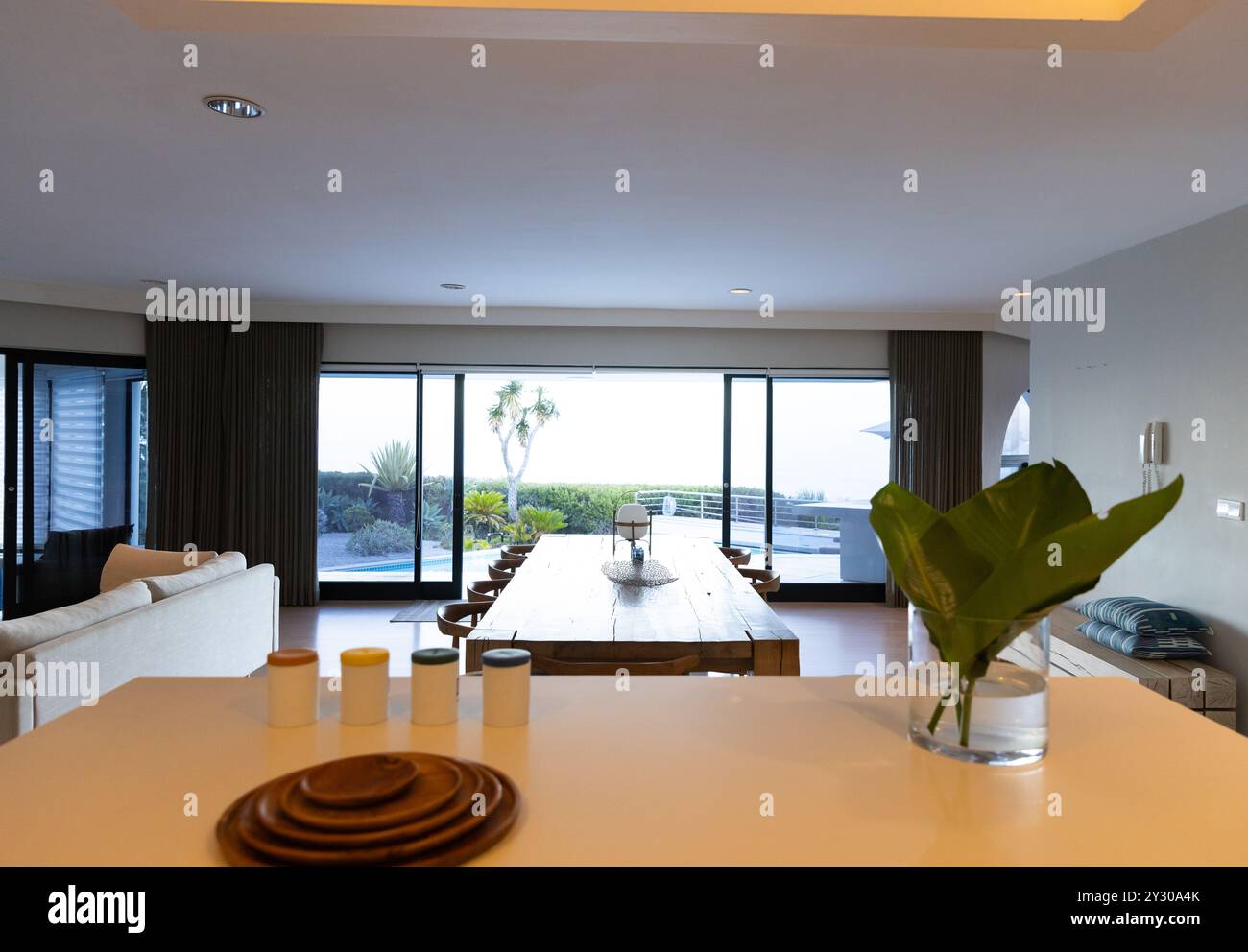 At home, Large dining table in modern living room with panoramic windows, creating serene ambiance Stock Photo