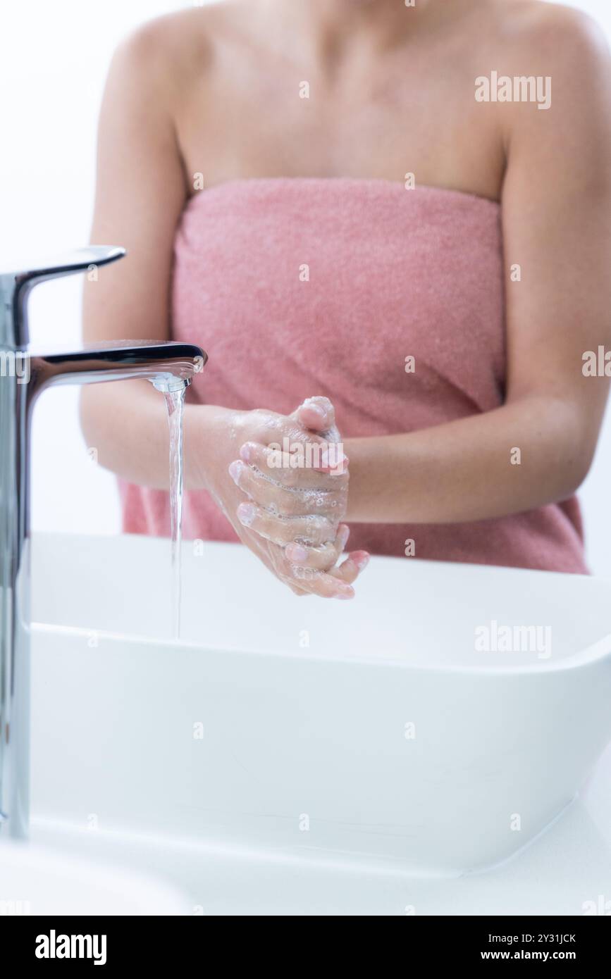 At home, Washing hands with soap, woman in towel at spa sink, maintaining hygiene Stock Photo