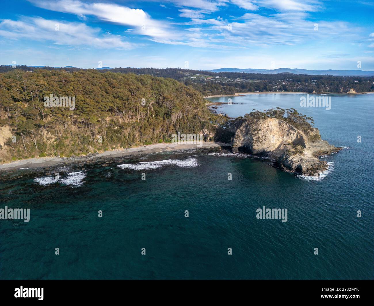 Aerial view of a coastal landscape with rocky cliffs, dense forest, and ...